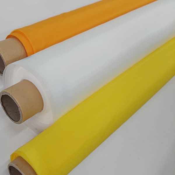 Três rolos de tela de nylon para serigrafia nas cores laranja, branco e amarelo dispostos em diagonal sobre fundo branco, evidenciando a textura do tecido.