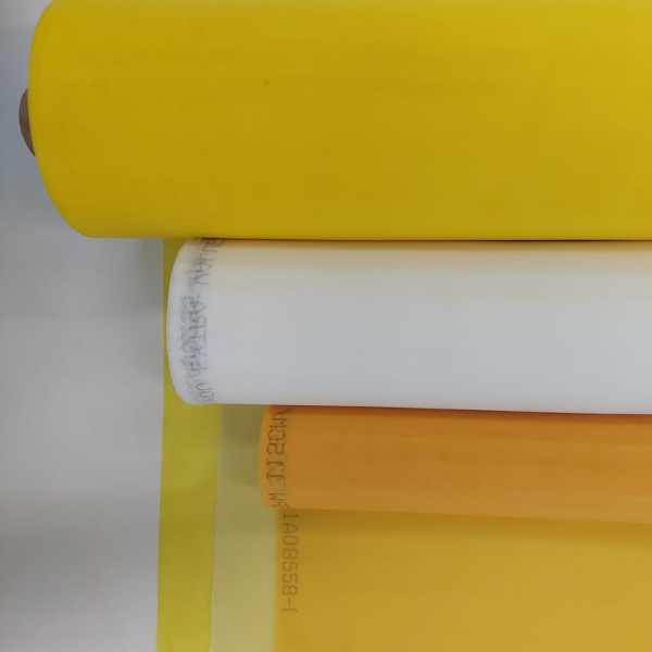 Rolos de tela de poliéster para serigrafia nas cores amarelo, branco e laranja posicionados em camadas, com o tecido amarelo aberto sobre a mesa.