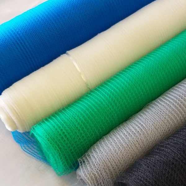 Rolos de tela antigranizo colorida alinhados em azul, branco, verde, cinza e preto, em close sobre superfície clara.