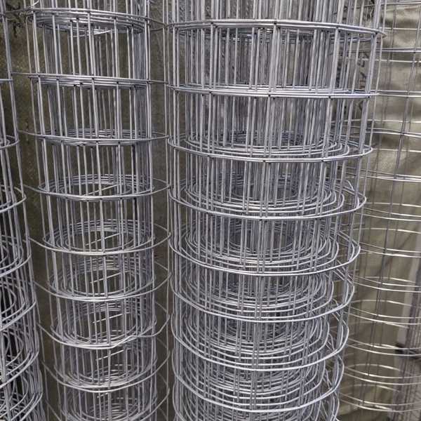 Conjunto de rolos de tela soldada galvanizada empilhados verticalmente, com fios metálicos brilhantes e malha regular. A imagem mostra o aspecto industrial e a resistência do material utilizado em estruturas e contenções.