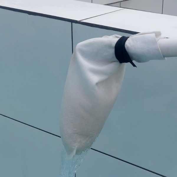 Bag de feltro branco instalado na saída de um tubo de água, preso com abraçadeira, filtrando a água que entra no tanque de cultivo de peixes ou camarão.