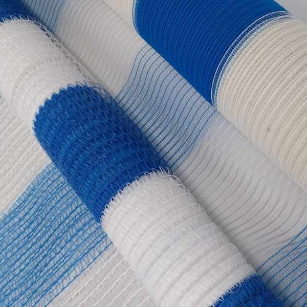 Detalhe de rolos de tela plástica azul e branca, com faixas alternadas e trama vazada, usados como tapume ou cerca de proteção.